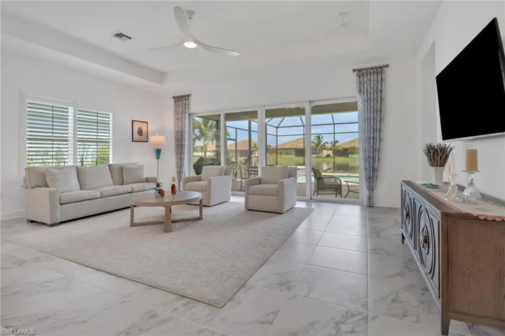 Tiled living room with ceiling fan, plenty of natural light, and a tray ceiling