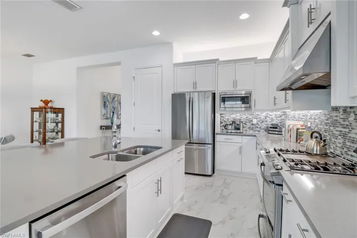 Kitchen with light tile patterned flooring, sink, decorative backsplash, white cabinetry, and stainless steel appliances