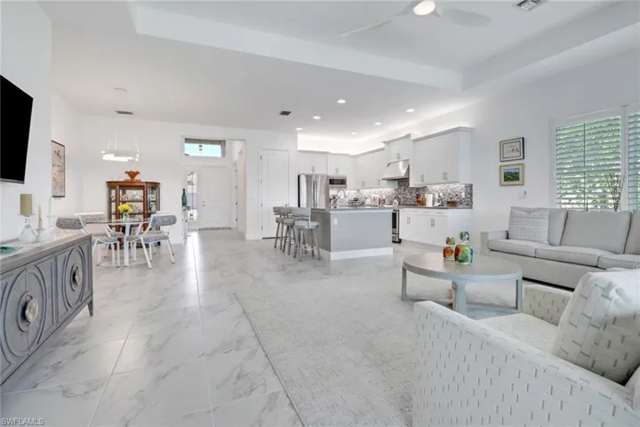 Living room with light tile patterned floors, sink, ceiling fan, and a tray ceiling
