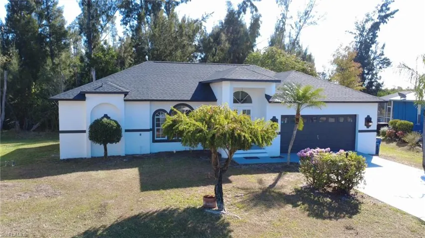 View of front facade with roof with shingles, a front lawn, driveway, and stucco siding