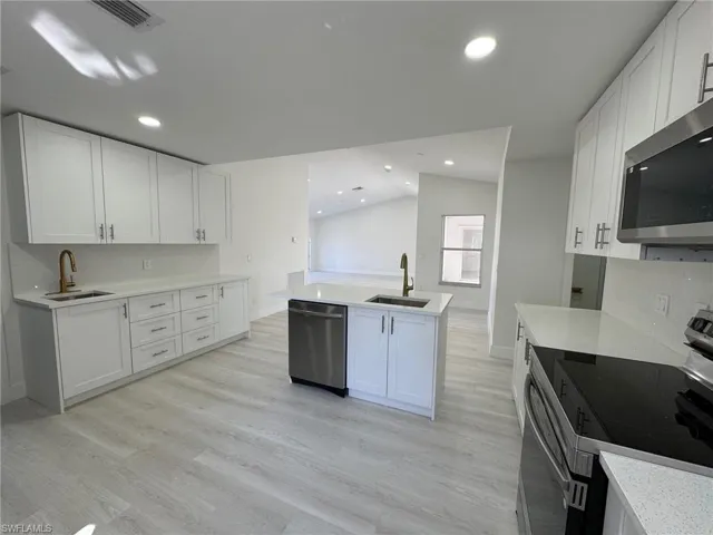 Kitchen with appliances with stainless steel finishes, backsplash, white cabinetry, vaulted ceiling, and a kitchen island with sink
