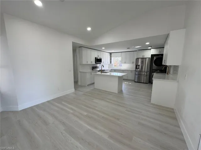 Kitchen featuring lofted ceiling, stainless steel appliances, stacked washing machine and dryer, white cabinets, and light wood finished floors