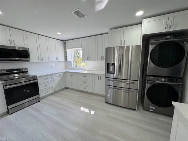 Kitchen featuring appliances with stainless steel finishes, open shelves, white cabinetry, stacked washer / dryer, and light wood-style flooring