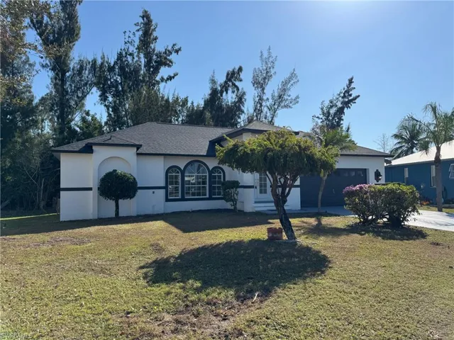 Ranch-style house with a front yard, stucco siding, a shingled roof, and driveway