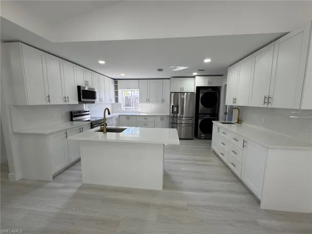 Kitchen featuring appliances with stainless steel finishes, stacked washing machine and dryer, light wood finished floors, decorative backsplash, and white cabinets