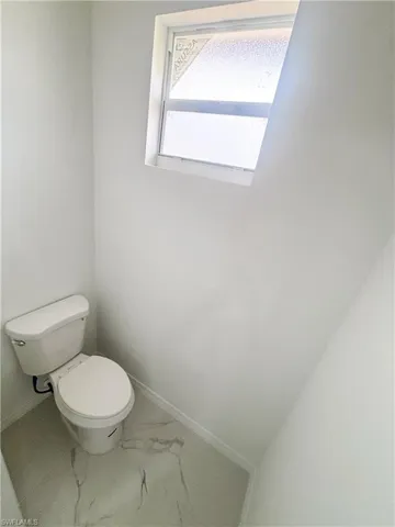 Bathroom with toilet, marble look tile flooring, and baseboards