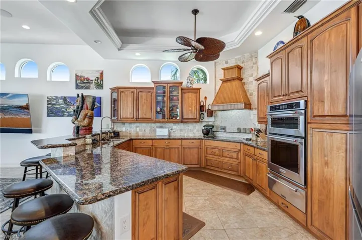 Kitchen featuring brown cabinets, a kitchen breakfast bar, dark stone countertops, decorative backsplash, and recessed lighting