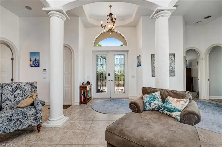 Tiled entryway with arched walkways, a towering ceiling, french doors, ornate columns, and a raised ceiling