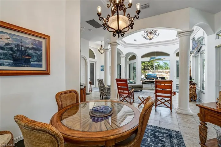 Tiled dining area with decorative columns, arched walkways, a high ceiling, and a chandelier