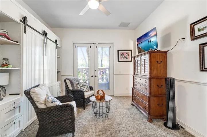 Living area with a barn door, light colored carpet, ceiling fan, and french doors