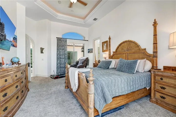 Bedroom featuring a raised ceiling, light carpet, a ceiling fan, arched walkways, and crown molding