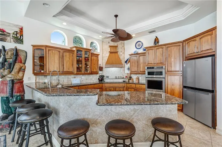 Kitchen with dark stone counters, brown cabinets, glass insert cabinets, and tasteful backsplash