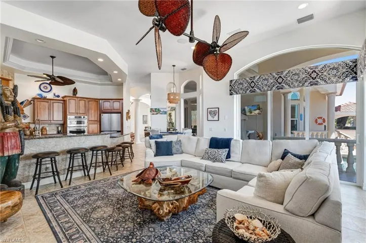 Living area featuring light tile patterned flooring, recessed lighting, ceiling fan, a tray ceiling, and a towering ceiling