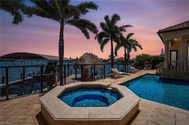 Pool at dusk with a water view, an in-ground hot tub, and a patio