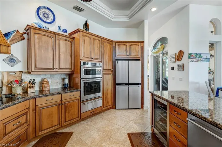 Kitchen with appliances with stainless steel finishes, dark stone countertops, brown cabinets, crown molding, and recessed lighting