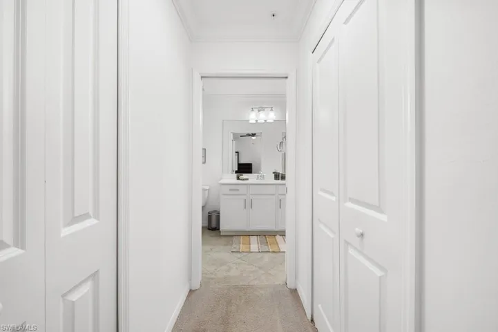 Corridor with ornamental molding, light carpet, and light tile patterned floors
