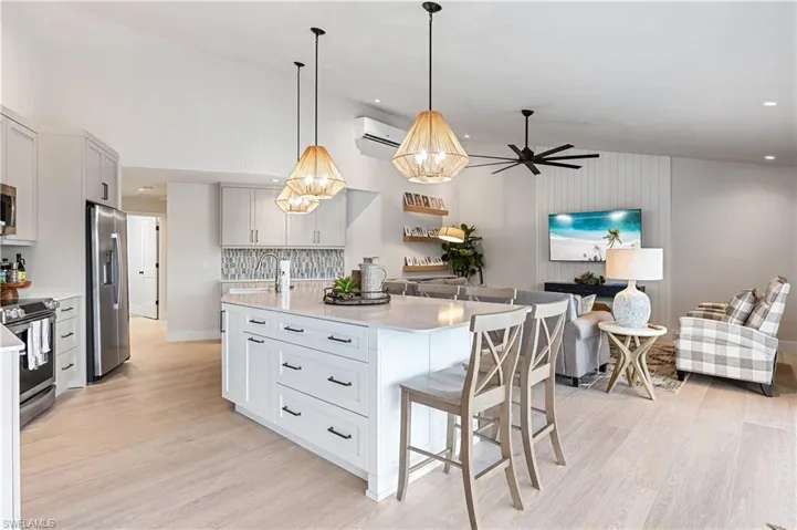 Kitchen featuring appliances with stainless steel finishes, light stone counters, pendant lighting, a wall unit AC, and a center island with sink