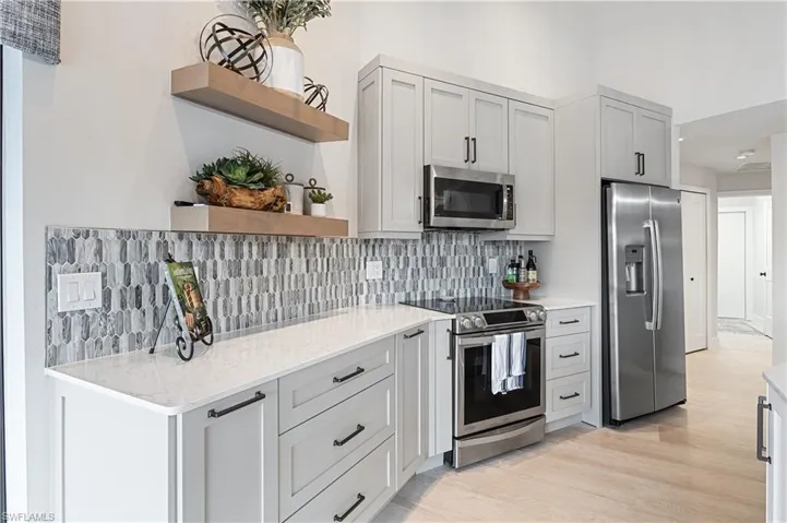 Kitchen featuring light stone counters, appliances with stainless steel finishes, decorative backsplash, and light hardwood / wood-style flooring