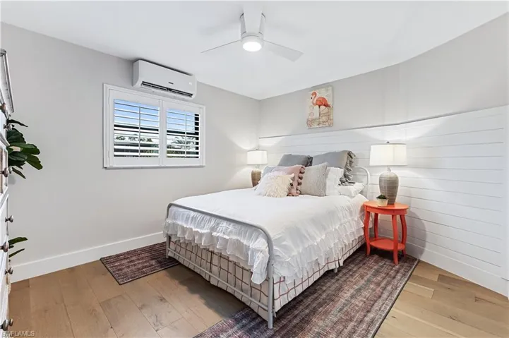 Bedroom with wood flooring, a wall unit AC, and ceiling fan