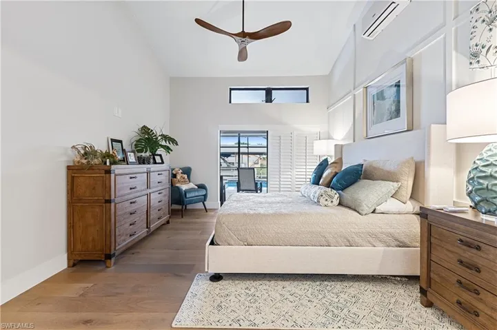 Bedroom featuring a high ceiling, genuine wood floors, an AC wall unit, and ceiling fan