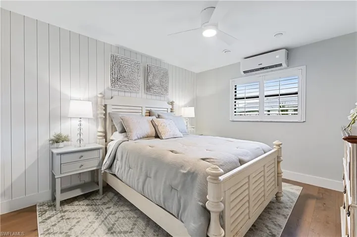 Bedroom with ceiling fan, a wall unit AC, and wood flooring
