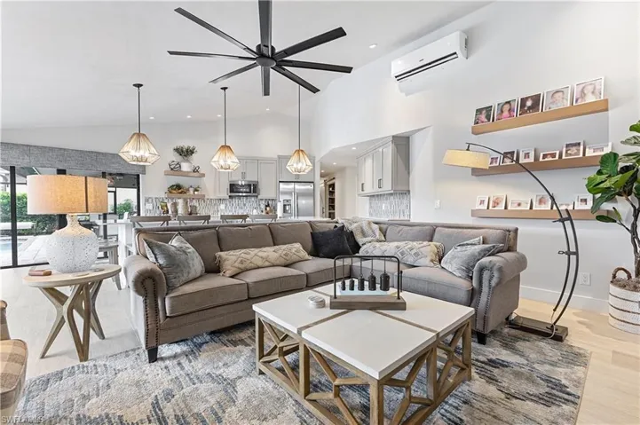 Living room with high vaulted ceiling, light wood-type flooring, ceiling fan, and a wall mounted AC