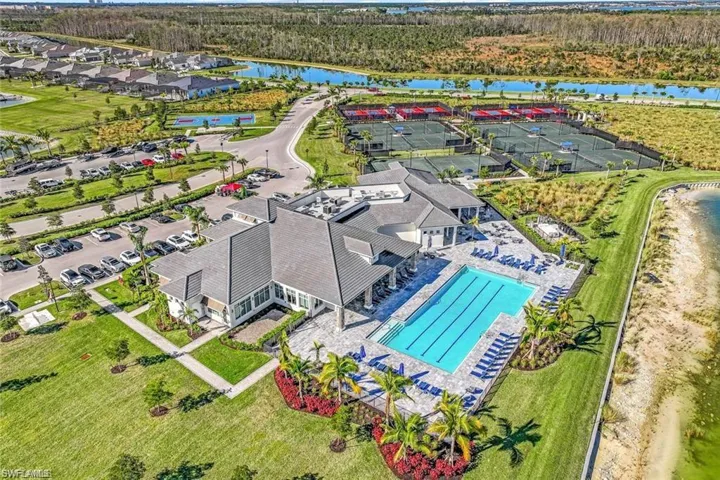 Community clubhouse with a large outdoor swimming pool, adjacent tennis courts, and landscaped grounds