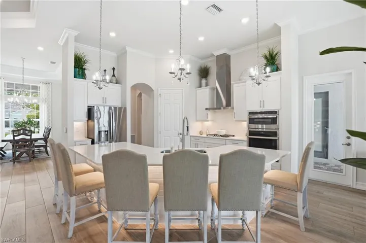 Gourmet kitchen featuring a large island, contemporary pendant lighting, stainless steel appliances, stacked wall oven, and wood-finish flooring