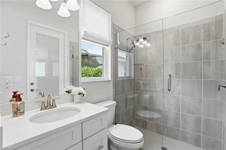 Tiled shower with a clear glass enclosure and built-in shelving, complemented by a white vanity with an undermount sink and polished chrome faucet