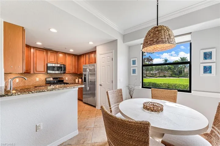 Kitchen with ornamental molding, stainless steel appliances, light tile patterned floors, decorative light fixtures, and light stone countertops