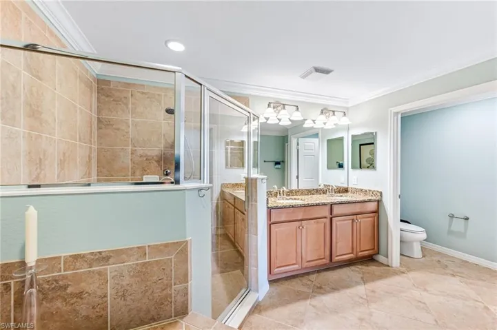 Bathroom featuring ornamental molding, a shower with door, vanity, and toilet