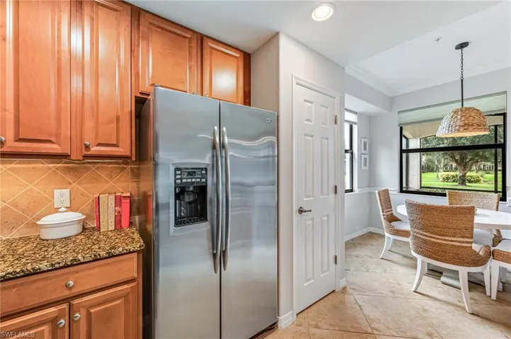 Kitchen with dark stone countertops, crown molding, stainless steel fridge, and tasteful backsplash