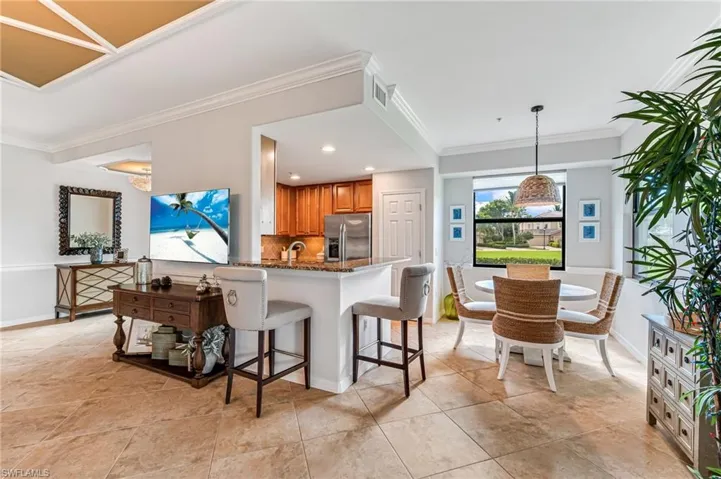 Kitchen with kitchen peninsula, decorative backsplash, crown molding, dark stone countertops, and stainless steel fridge
