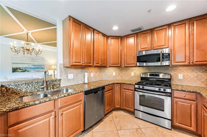 Kitchen with appliances with stainless steel finishes, backsplash, stone countertops, sink, and a chandelier