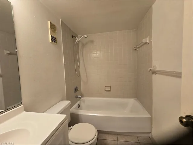 Full bathroom with toilet, tiled shower / bath combo, tile floors, and vanity