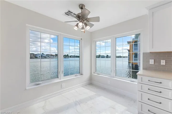 Unfurnished dining area with a water view, light marble finish floors, and a ceiling fan