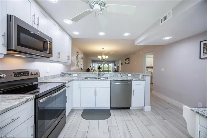 Kitchen featuring ceiling fan with notable chandelier, appliances with stainless steel finishes, white cabinetry, and kitchen peninsula
