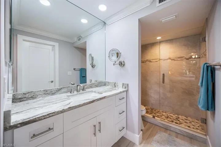 Bathroom with vanity, wood-type flooring, walk in shower, toilet, and ornamental molding