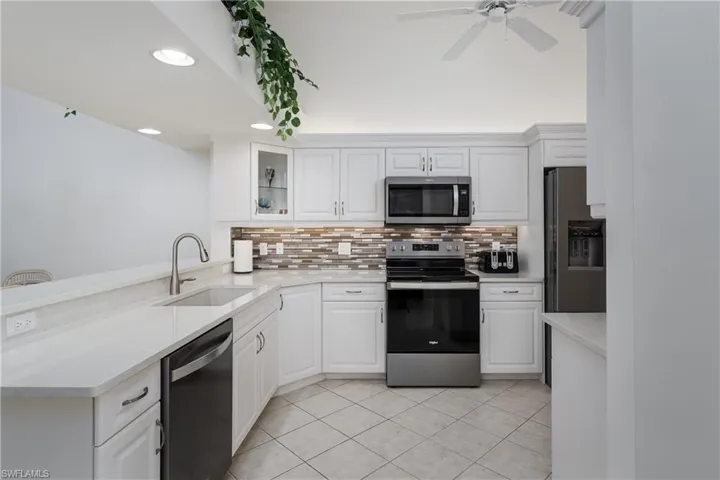 Bright kitchen featuring white cabinetry, light-toned countertops, a mosaic tile backsplash, stainless steel appliances, and diagonal tile flooring