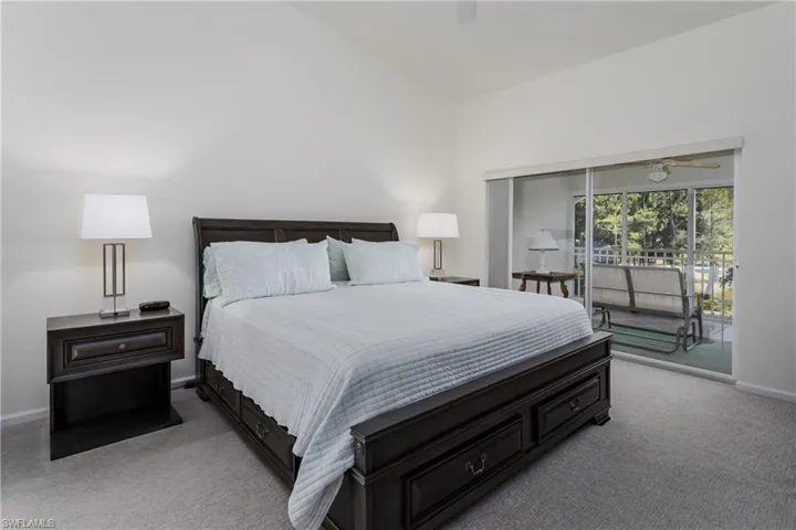 Bedroom featuring vaulted ceilings, plush carpet flooring, and direct access to an enclosed porch with tree-lined scenery