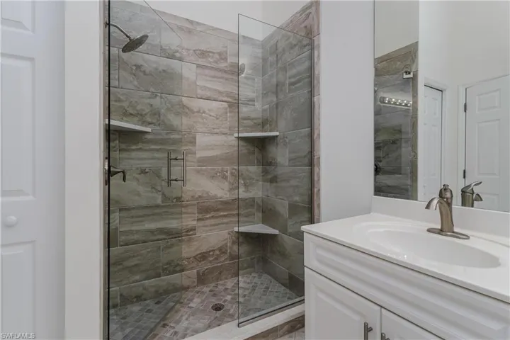 Tiled shower enclosure with a glass door, rain showerhead, and integrated corner shelving