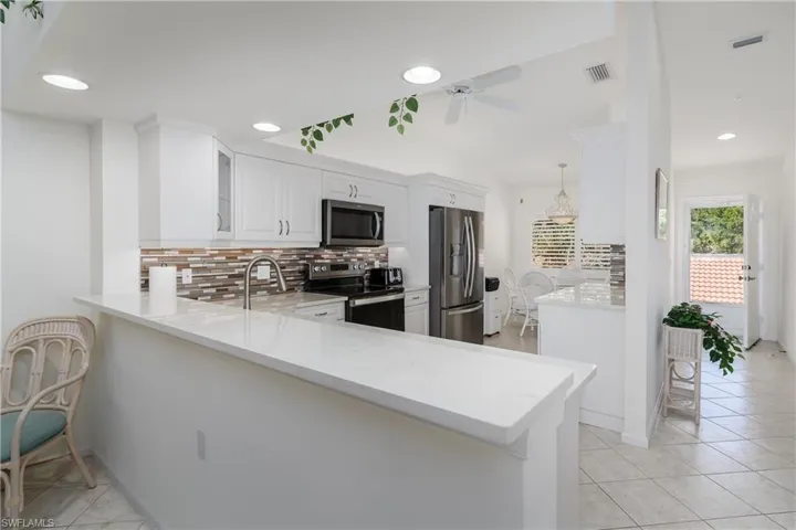 Well-appointed kitchen featuring white cabinetry, stainless steel appliances, a multi-tone tile backsplash, and a breakfast bar with a light-toned countertop