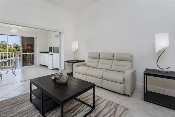 Vaulted ceiling living area featuring tile flooring, white walls, and sliding glass doors opening to a balcony