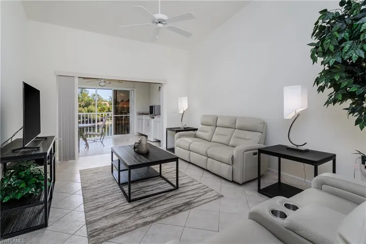 Vaulted ceilings enhance this living area featuring tile flooring, a ceiling fan, and sliding glass doors opening to a balcony with water views