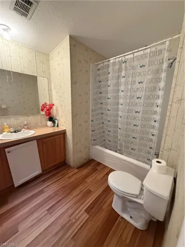 Bathroom with shower / bath combination with curtain, light wood-style flooring, vanity, wallpapered walls, and a textured ceiling