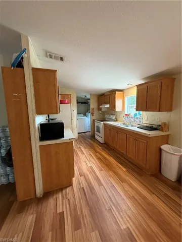 Kitchen featuring light wood-type flooring, light countertops, white range, a textured ceiling, and washer and dryer