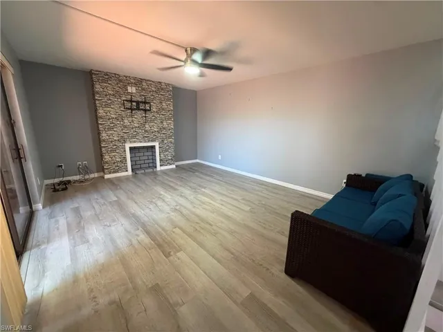 Spacious interior featuring wood-finish flooring, a stacked stone fireplace surround with a white mantel, and a ceiling fan with integrated lighting
