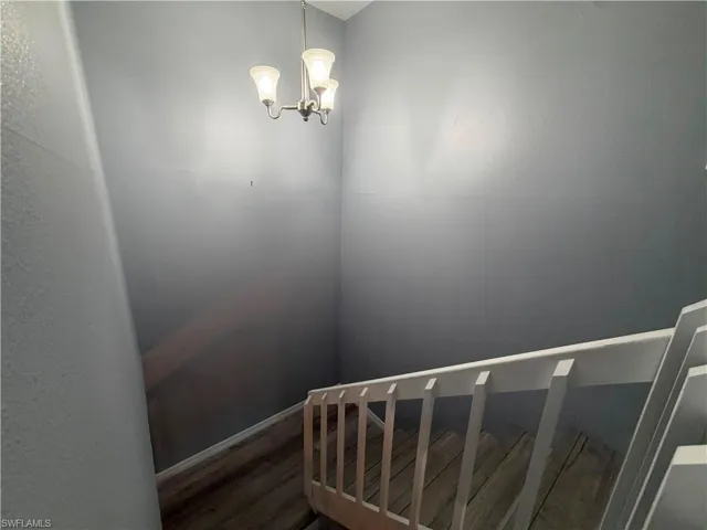 Staircase featuring wood-finish treads, a white painted railing, and a brushed nickel chandelier with frosted glass shades