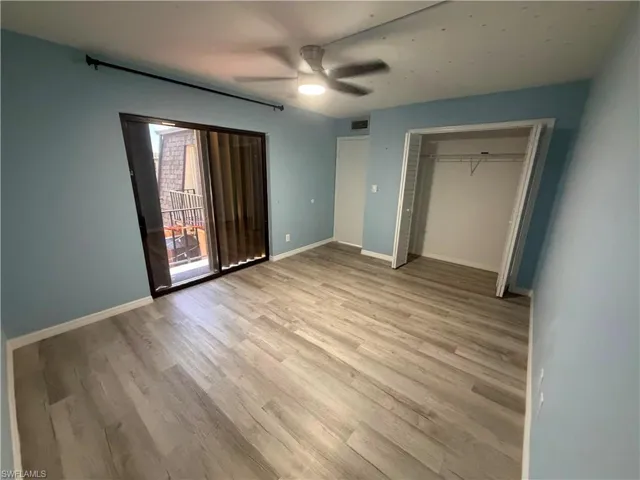 Spacious room featuring wood-finish flooring, a ceiling fan, sliding glass door access to an exterior space, and an open closet with wire shelving