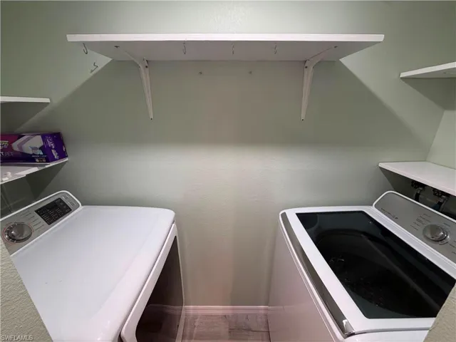 Dedicated utility space featuring light green walls, a top-mounted white shelf with hooks, and wood-finish flooring